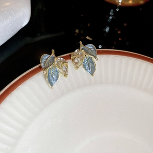 Macro detail of leaf studs with blue enamel and sparkling zircon on golden base