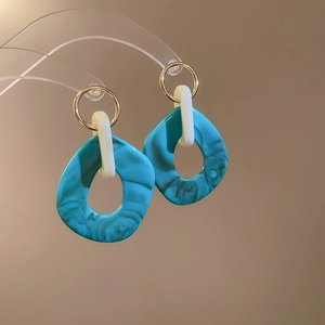 Macro view of blue-green marble textured irregular earrings with golden metal rings