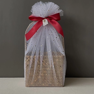 Detail of seagrass gift basket wrapped in star pattern tulle with a red ribbon bow