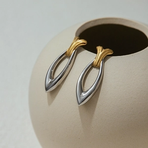 Two-tone 18K stainless steel hollow teardrop earrings on a beige ceramic vase