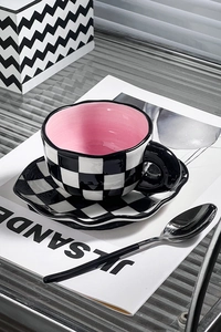 Detail of checkered ceramic coffee mug and saucer with pink glaze and matching spoon