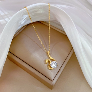 Macro view of gold swan necklace with large zircon pendant on white silk fabric