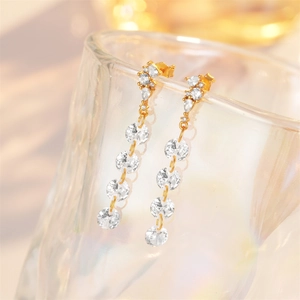 Macro shot of gold tassel earrings with sparkling crystals hanging on a glass rim