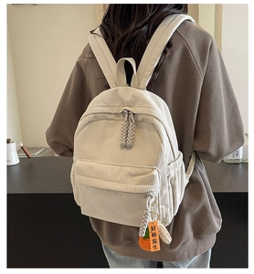 Detail of off-white corduroy backpack featuring a creative orange persimmon charm