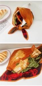 Detail of accordion pleated square scarf featuring vibrant orange floral print and soft texture