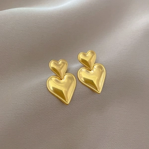 Polished gold double heart stud earrings on elegant grey silk background