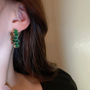 Primo piano di orecchini con smeraldo verde in castone dorato indossati da modella
