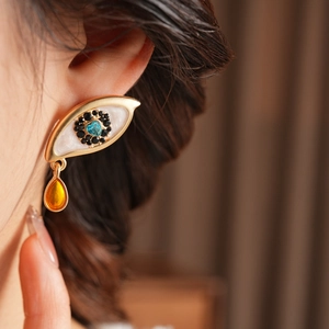 Detail view of vintage eye-shaped earring with blue heart gem and yellow teardrop charm