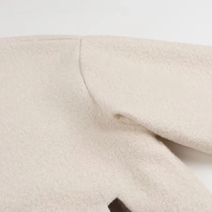 Gros plan sur la texture douce du lainage beige et la couture d'épaule du manteau ample