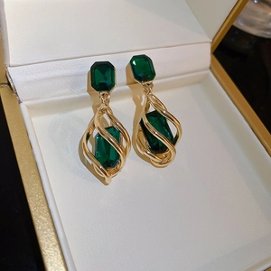 Close-up of gold drop earrings with green rectangular and pear-shaped gemstones