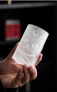 Macro detail of hand-held frosted glass cup with embossed cat and pumpkin relief