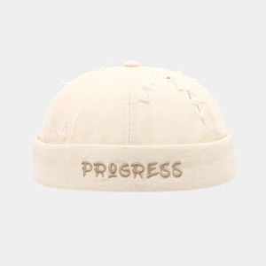 Gros plan sur la broderie PROGRESS et les détails usés du bonnet docker crème