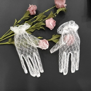 Close-up of white lace bridal gloves with ruffled wrist detail on a black surface