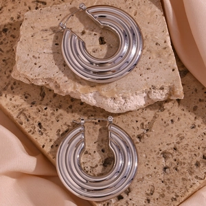 Detail of silver textured hoop earrings with vertical ribbing on a stone surface