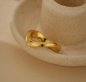 Macro shot of gold irregular wave ring on beige ceramic plate for minimal style