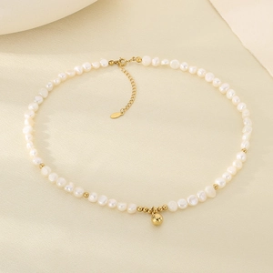 Dettaglio della collana vintage in titanio con perle e perline dorate su sfondo crema