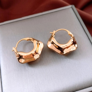 Close-up of 18K gold plated irregular wavy hoop earrings on a textured jewelry box