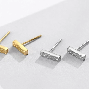 Detailed macro shot of geometric rectangular stud earrings with hammered metal texture