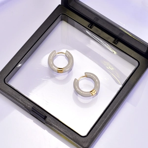 Détail de boucles d'oreilles anneaux en émail doré présentées dans un cadre flottant noir
