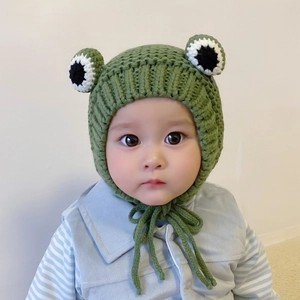 Detail of green knit baby hat with crochet frog eyes and warm ear protection