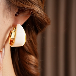 Close-up of a C-shaped gold-plated earring with white resin inlay worn by a model