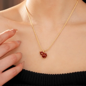 Close-up of a 18k gold-plated gourd pendant necklace with red enamel worn by a model