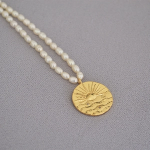 Macro shot of gold coin pendant with sun relief and natural white freshwater pearls