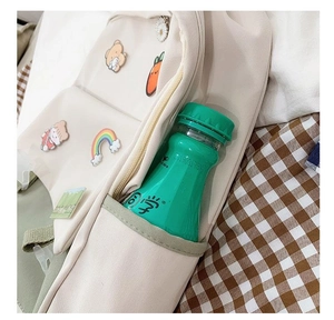 Detail of canvas backpack side pocket showing capacity for water bottles and cute patches