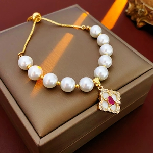 Detail of gold flower tassel bracelet with white pearls and red clover charm