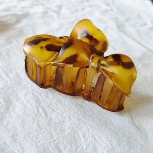Detail of amber tortoiseshell hair claw clip on soft white fabric background textures