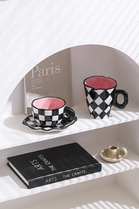 Detail of pink-glazed ceramic mug and saucer set with black and white checkerboard pattern