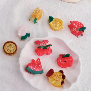 Vibrant fruit-shaped PVC hair clips set on white tray including watermelon and cherry