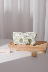 Detailed close-up of green leaf embroidery on a cream linen cosmetic bag with a small tag