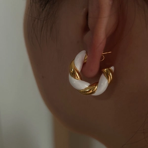Close-up of twisted gold plated earrings with white enamel finish on female model