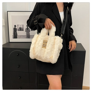 Detail of off-white plush tote bag with black strap worn over a black blazer