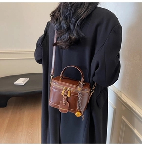 Brown vintage box bag with gold hardware shown as a crossbody on a black coat back
