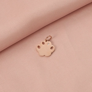 Macro view of rose gold paw-shaped pendant with a sparkling gemstone on pink fabric