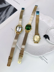 Three vintage oval quartz watches with gold mesh straps shown on a white platter