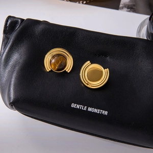 Macro shot of gold tiger eye studs on a black leather pouch with brand lettering