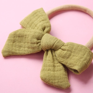 Close-up of olive green cotton muslin bow with soft beige nylon headband on pink background