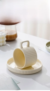 Detail of creamy yellow ceramic coffee cup set with square handle and ribbed texture