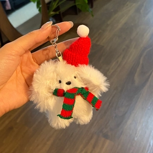 Plush white dog keychain with red Christmas hat and striped scarf held in hand