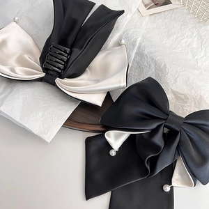 Elegant satin bow hair clips in black and cream contrast with pearl accents on white paper
