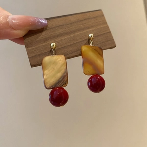 Macro shot of square shell earrings with red beads and gold metal accents