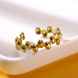 Macro shot of gold-plated stainless steel beaded ring with open design on white tray