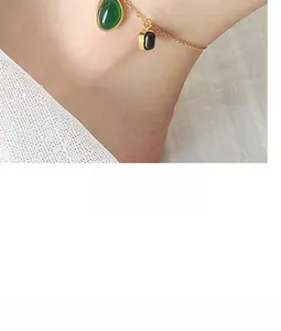 Detailed shot of vintage gold anklet with green teardrop and black rectangular pendants