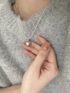 Detail view of large grey pearl pendant on silver snake chain worn on grey sweater