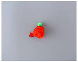 Detailed view of mini knitted hat hair clip with orange yarn and green pompom