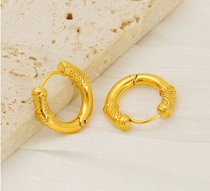 Close-up of gold hoop earrings with embossed cloud pattern on silk and stone base