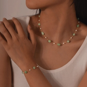 Detail of gold necklace and bracelet set with light green stones and white pearls